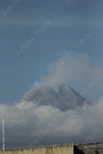 Merapi Mountain shrouded in white clouds against a blue sky background