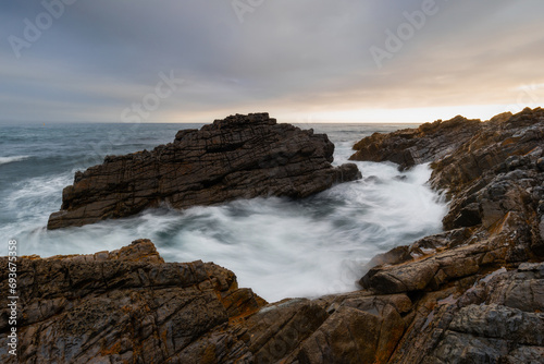 Wave flowing between two big rocks on the coastline.