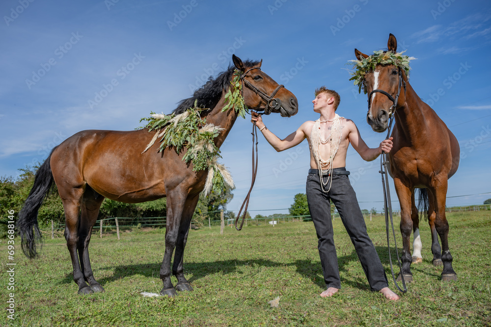 Jeune homme torse nu avec deux chevaux ornés de couronnes de fleurs et de feuilles