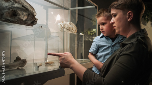 Curious little boy in his mothers arms looking at an animal skeleton in a bone display case at a natural history museum exhibition. photo