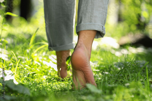 Woman walking barefoot on green grass outdoors, closeup photo
