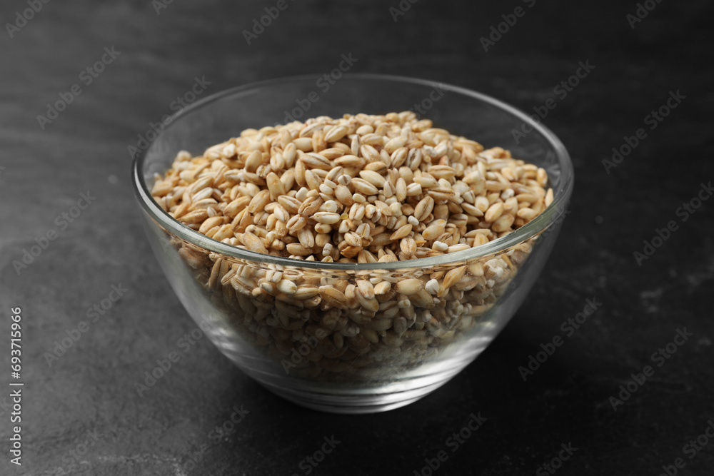 Dry pearl barley in bowl on dark gray table, closeup