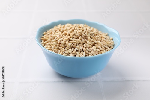 Dry pearl barley in bowl on white tiled table, closeup