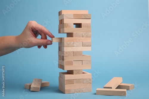 Woman playing Jenga on light blue background, closeup photo