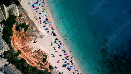 Aerial view of tropical beach with azure transparent sea water, sand, colorful umbrellas 