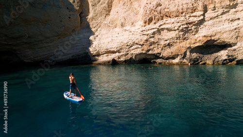View of surfer on board in turquoise water in front of big cliff