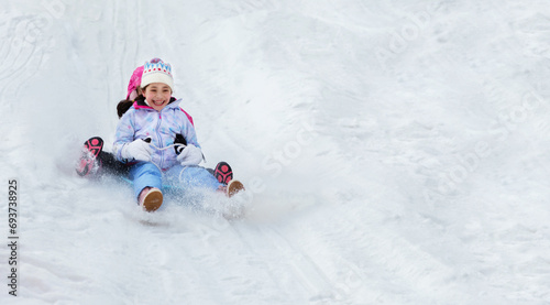 Little girls are sledding down snow slide. Having fun in the winter, fun vacations.