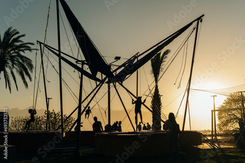 children jumping in trampoline high into the sunset sky safed with elastic safety belt