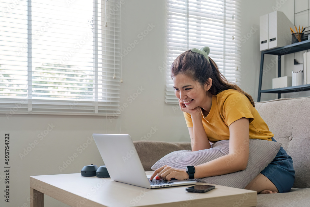 Beautiful Asian woman wearing casual clothes On the sofa using a laptop computer, entertaining with social media, relaxing, smiling and laughing. Beautiful Asian woman wearing casual clothes On the sofa using a laptop computer, entertaining with social media, relaxing, smiling and laughing.