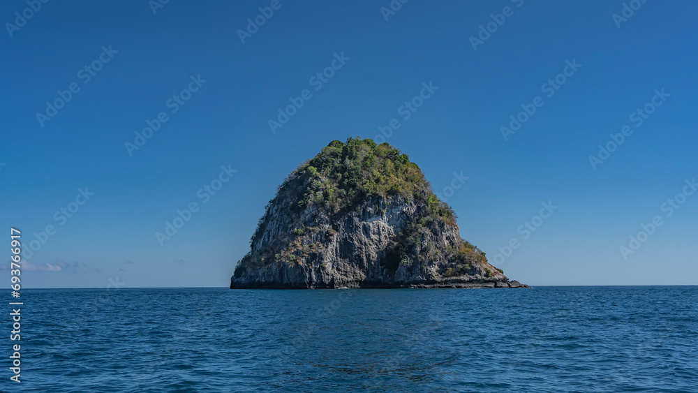 An island in the Indian  ocean. Steep rocky slopes covered with green vegetation rise above the blue water. Clear azure sky. Madagascar. Nosy Kivinjy.   