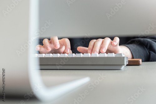 Manos de mujer tipeando con un teclado gris frente al ordenador. photo