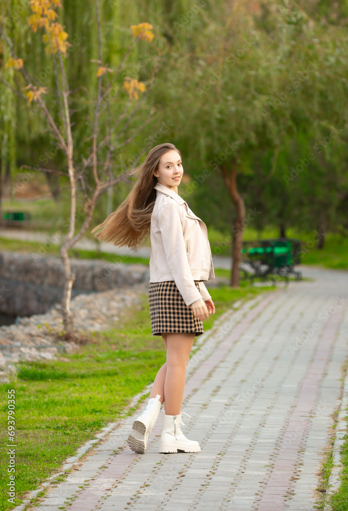 A young smiling girl walking in an autumn park in a good mood. Teenage girl, portrait against a background of nature. Fashion style trend.