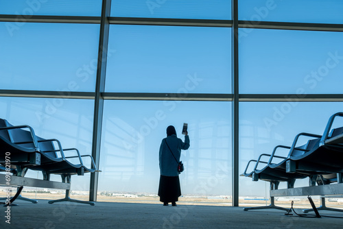 Female holding her passport behind airport waiting seats and in front of windows