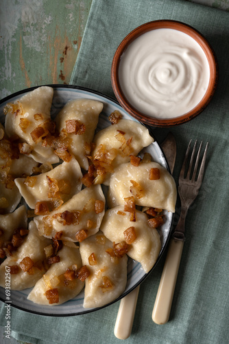 Traditional Ukrainian food - dumplings varenik with sour cream close up. Fried bacon and onion covers them on top. Food photography photo
