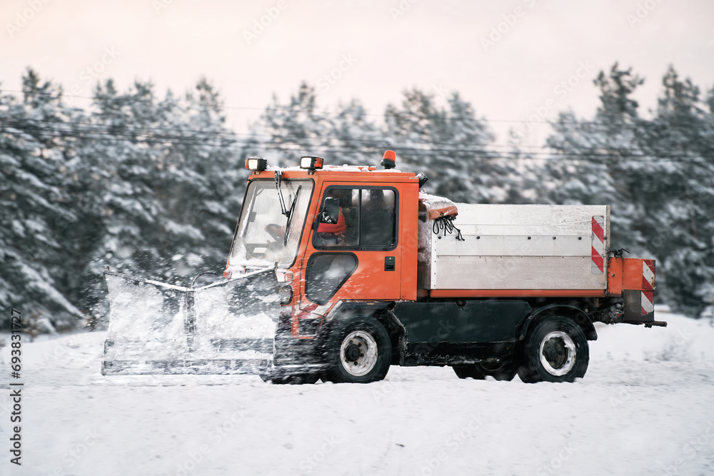 Tractor with mounted salt and sand spreader, road maintenance - winter gritter vehicle. Municipal service melting ice and snow on streets. Diffusing salt blend on  public roads.