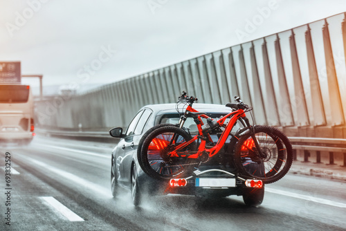 A car with a rack of full-suspension mountain bikes mounted on the trunk travels on the highway for a family vacation and adventure. MTB extreme riding.