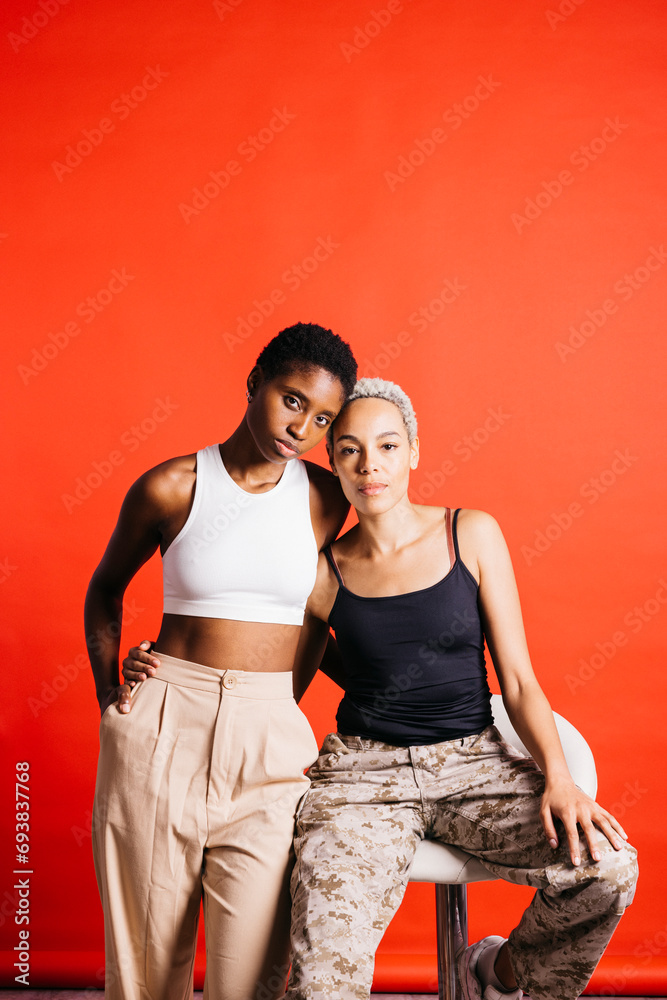 Naklejka premium Portrait of a young female couple in front of a red background at studio. Two women together at studio.