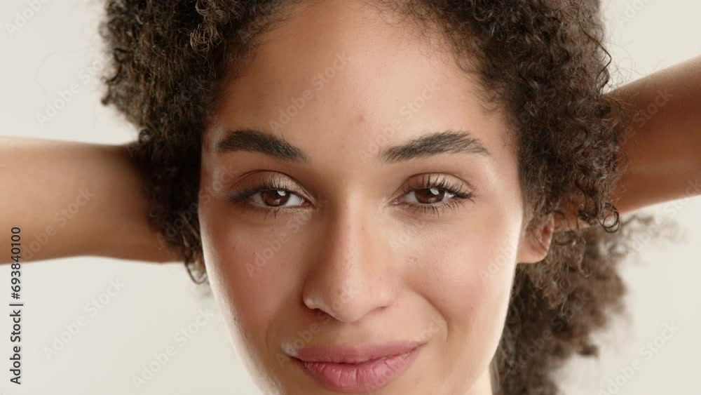 Close up of pretty female face, natural beauty of young lady holding afro curls with hands, smiling, flirting, casting sexy glances from side to side. High quality 4k footage Close up of pretty female face, natural beauty of young lady holding afro curls with hands, smiling, flirting, casting sexy glances from side to side. High quality 4k footage