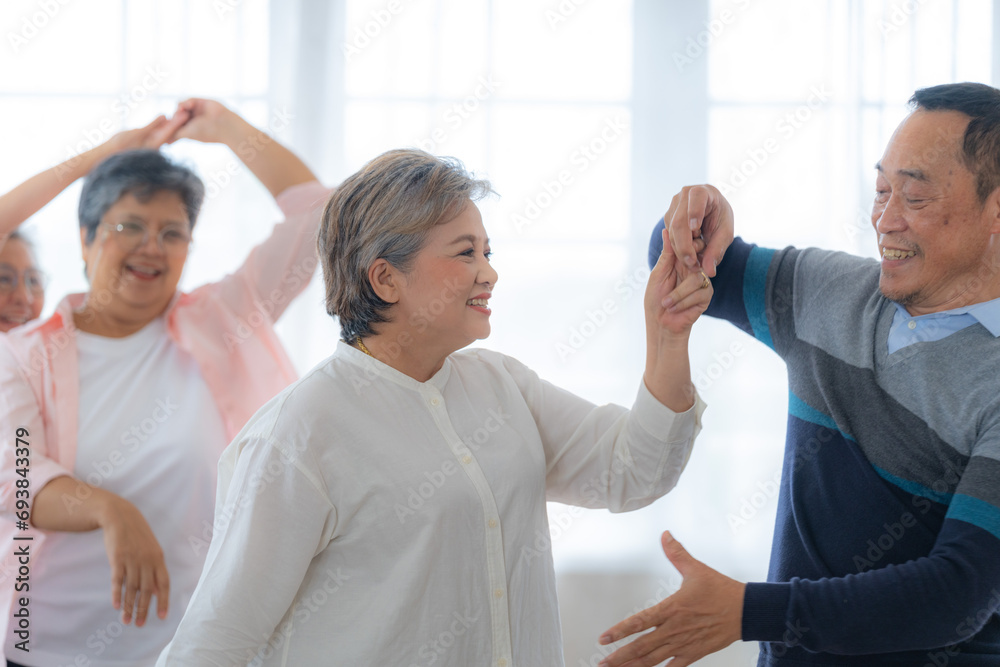 Obraz premium Asian Older male and females people dance with their partners on a dancing floor in living space. Happy older couple performing get exercise. Joyful carefree retired senior friends enjoying relaxation