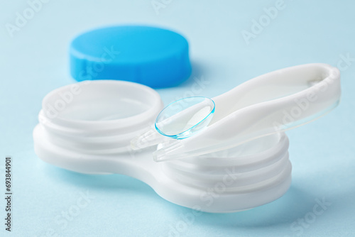 Contact lens on tweezer with container on light blue background
