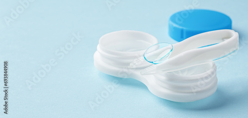 Contact lens on tweezer with container on light blue background