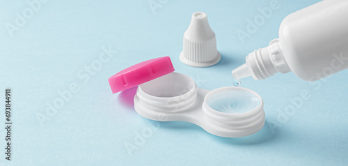 Pouring solution from bottle on contact lens in container on light blue background