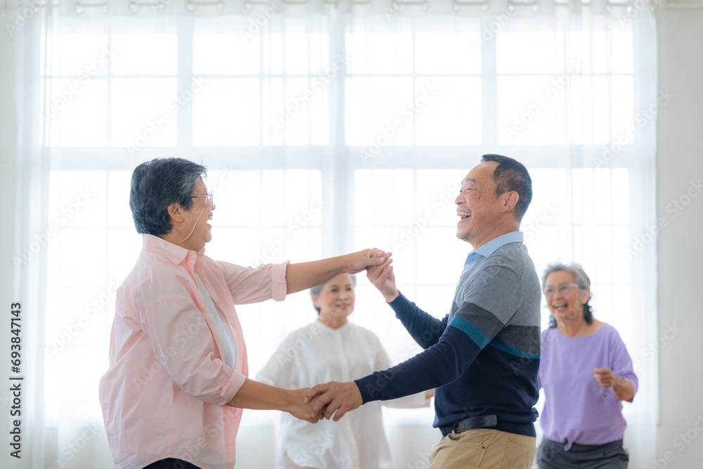 Obraz premium Asian Older male and females people dance with their partners on a dancing floor in living space. Happy older couple performing get exercise. Joyful carefree retired senior friends enjoying relaxation