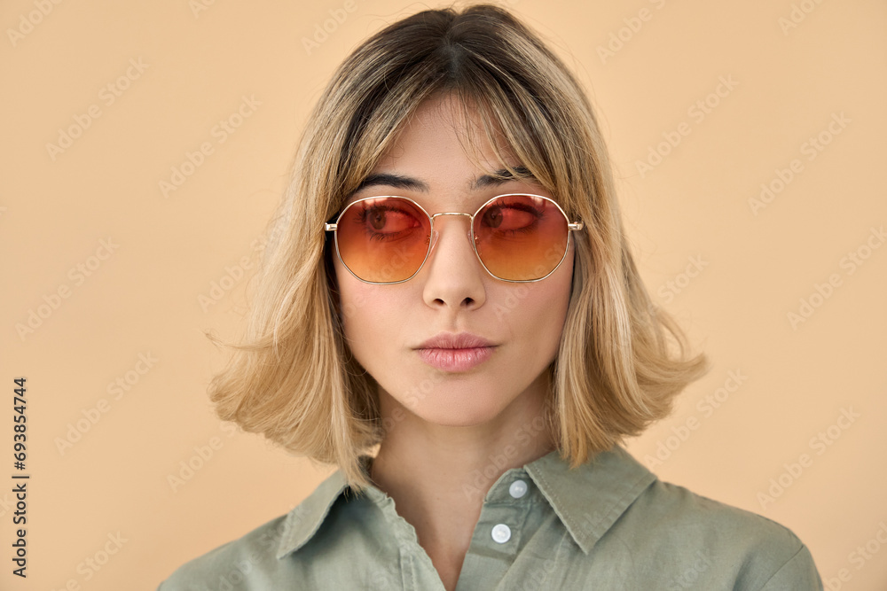 Pretty hipster gen z blonde young fashion woman, cool cute beautiful girl with short blond hair wearing trendy color sunglasses looking aside isolated on beige background. Close up face portrait. Pretty hipster gen z blonde young fashion woman, cool cute beautiful girl with short blond hair wearing trendy color sunglasses looking aside isolated on beige background. Close up face portrait.