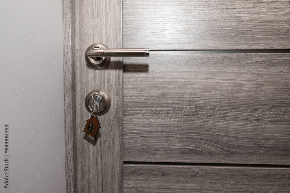 Buy Or Rent concept. Keys with trinket in shape of house in the door keyhole.