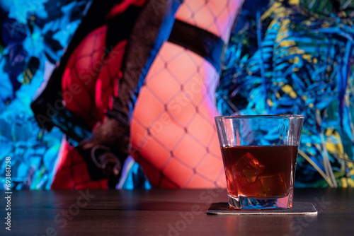 Glass of whiskey on the bar in front of the blur image Sexy woman in Thong. Lady with a leather whip. BDSM toys for role-playing sexual games with domination and submission photo