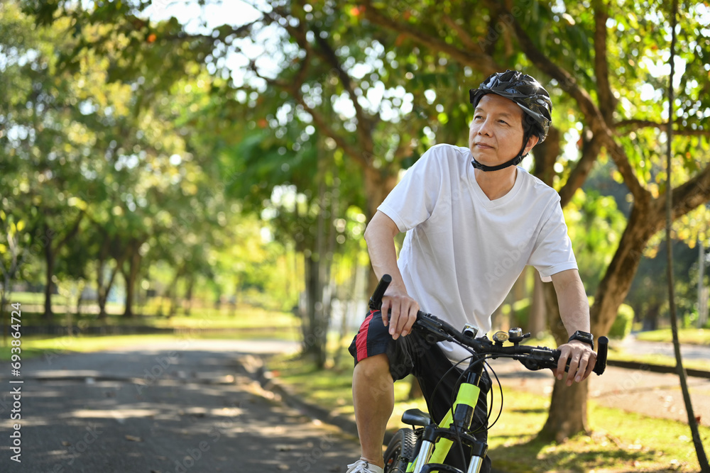 Obraz premium Active retired man in helmet riding bicycle in park on sunny summer day