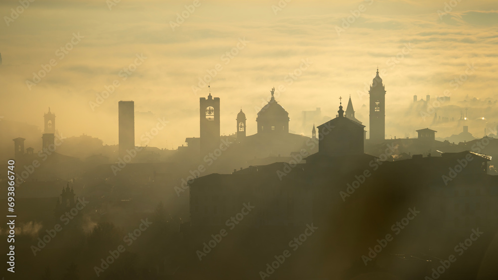 Bergamo, Italy. Amazing aerial landscape of the fog rises from the plains and covers the old town during sunrise. Warm colors. Bergamo one of the most beautiful city in Italy