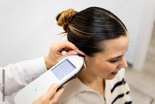 Zenithal view of an unrecognizable otolaryngologist uses a tympanometer on the ear of a pretty Caucasian girl to perform a hearing study. A device to detect alterations in the middle ear. photo