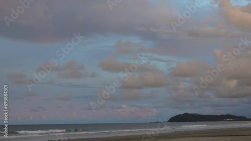 A romantic evening on the beach. The blue sky is highlighted with pink on the horizon. Picturesque cumulus clouds. The waves of the turquoise ocean roll towards the shore, foaming.  Malaysia. Borneo.