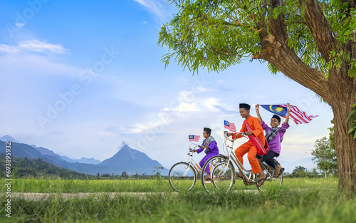independence Day concept - Two happy young local boy riding old bicycle at paddy field holding a Malaysian flag