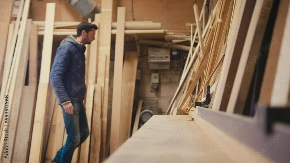 Male carpenter working in woodwork workshop choosing wood for project - shot in slow motion Male carpenter working in woodwork workshop choosing wood for project - shot in slow motion