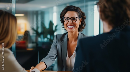Handshake between smiling businesswoman and client at office meeting. Mid aged female manager or hr hiring new recruit, bank or insurance agent, or lawyer making contract deal at work photo