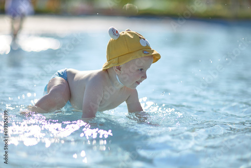 a little half a year old, a baby baby crawling on the water, smiling, outdoors, in a panama hat, in diapers, in the sun at the resort.