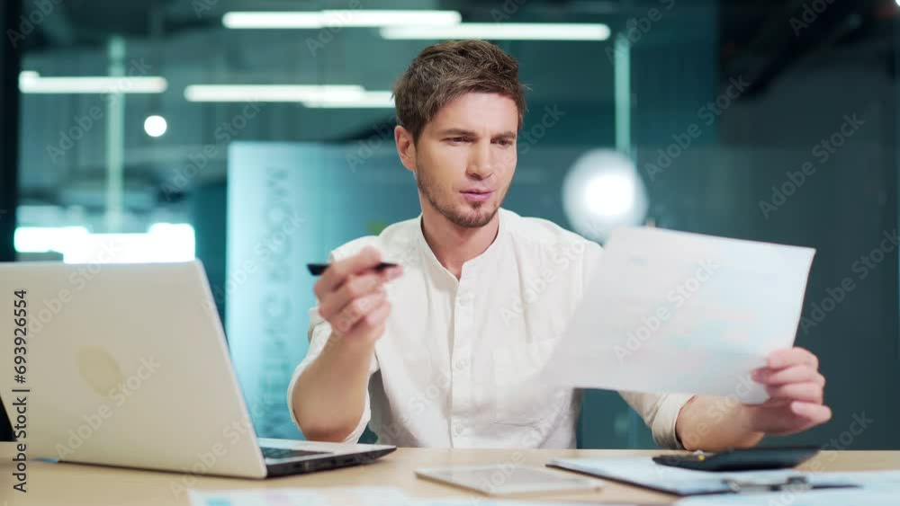 Young entrepreneur having difficulty with paper work sitting in office. Disgruntled financier holding documents, can't understand. Businessman freelancer not satisfied with the financial report Young entrepreneur having difficulty with paper work sitting in office. Disgruntled financier holding documents, can't understand. Businessman freelancer not satisfied with the financial report