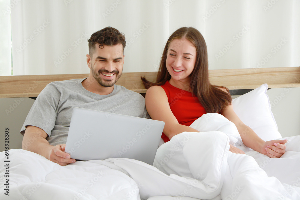 Smiling Caucasian Couple relaxing and watching movie online funny on laptop in social media technology in bedroom together. Work from home and lifestyle on holiday Concept Smiling Caucasian Couple relaxing and watching movie online funny on laptop in social media technology in bedroom together. Work from home and lifestyle on holiday Concept
