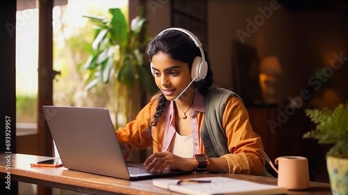 Young Indian woman studying online with laptop and notebook at home office. E-learning and remote work concept. photo