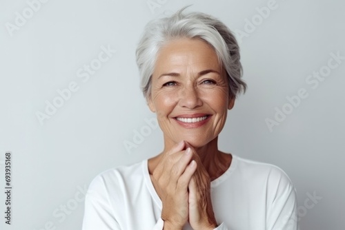 Portrait of beautiful mature woman with snow-white smile, gray hair on gray background. Middle-aged lady in light clothes, happy pensioner looking at the camera. Beauty, skin care concept photo