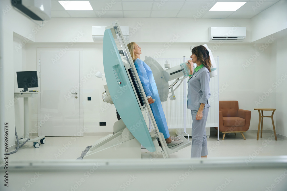 Wall Mural Experienced radiologic technologist preparing adult female for radiography