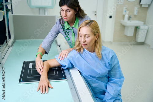 Experienced radiologic technologist preparing woman for upper limb radiography photo