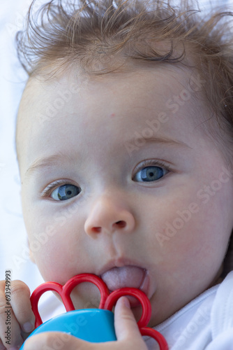 Adorable little 4-month baby holding toy teether near month. Baby face. White background.