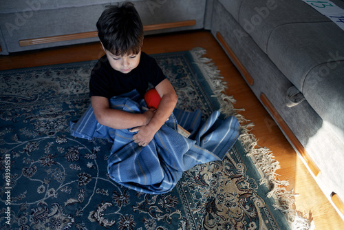 A boy with autism calms down, wrapped in his favorite blanket and sitting on the floor. photo