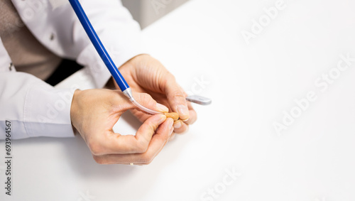 Photo of the hands of an otorhinolaryngologist using a stethoscope to listen to the sounds emitted by a behind-the-ear hearing aid. Hearing aid care concept.Checking the operation of your hearing aid. photo