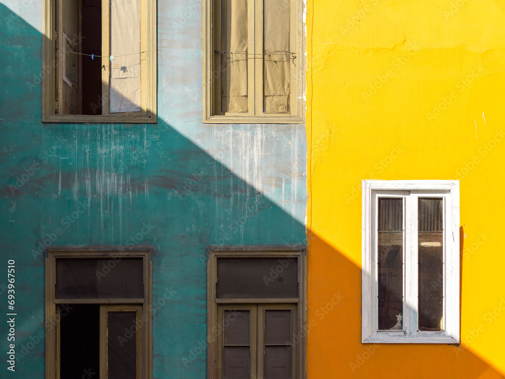 Artistic and abstract composition of a yellow and grey facade in Lima, Peru. Windows, oblique and diagonal shadow.