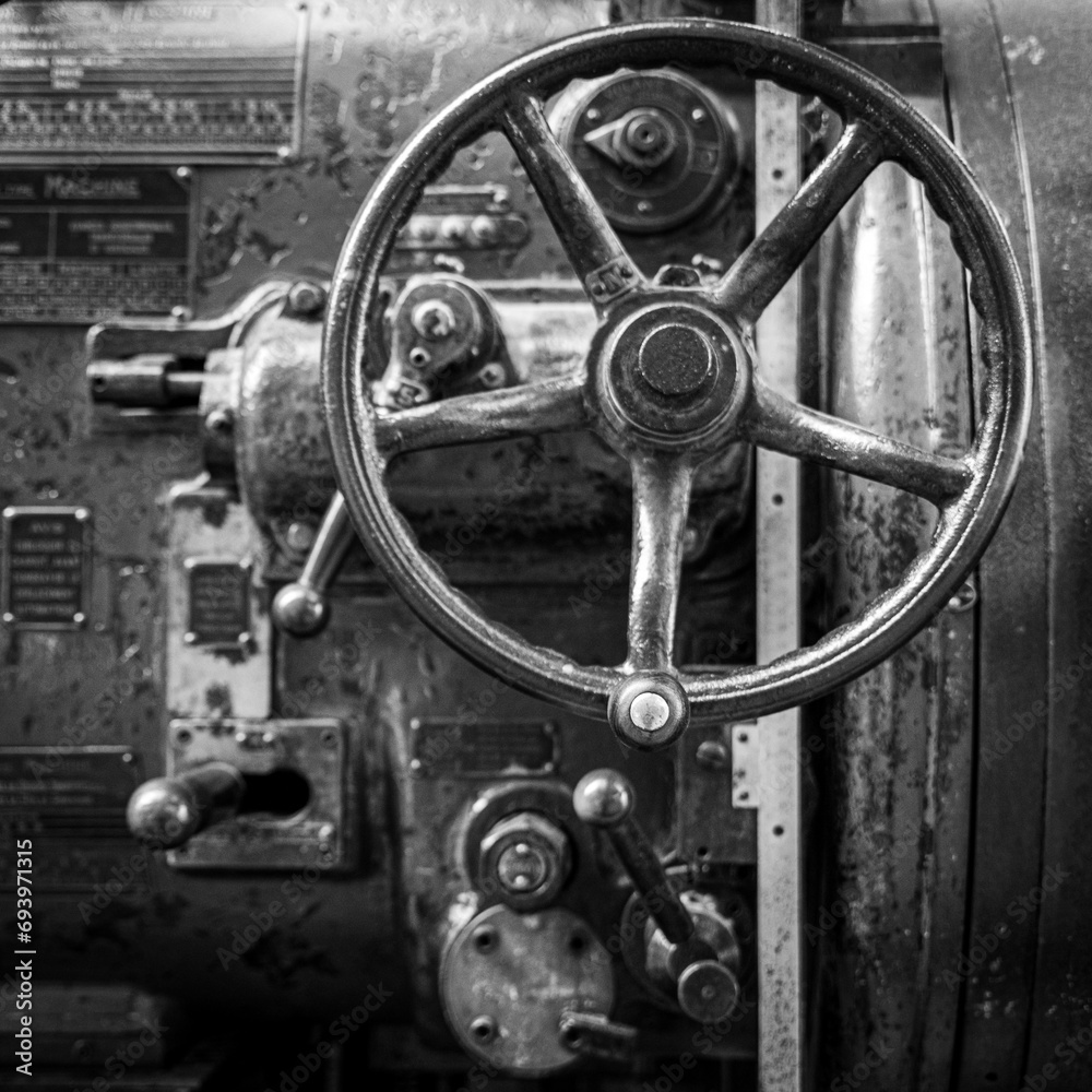 Obraz premium Flywheel of old industrial machine to raise or lower the pressure of a steam engine in black and white BW