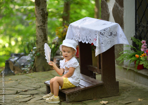Obraz na płótnie A little girl is sitting in the forest and waving a cloth fan in front of her to cool off w salonie